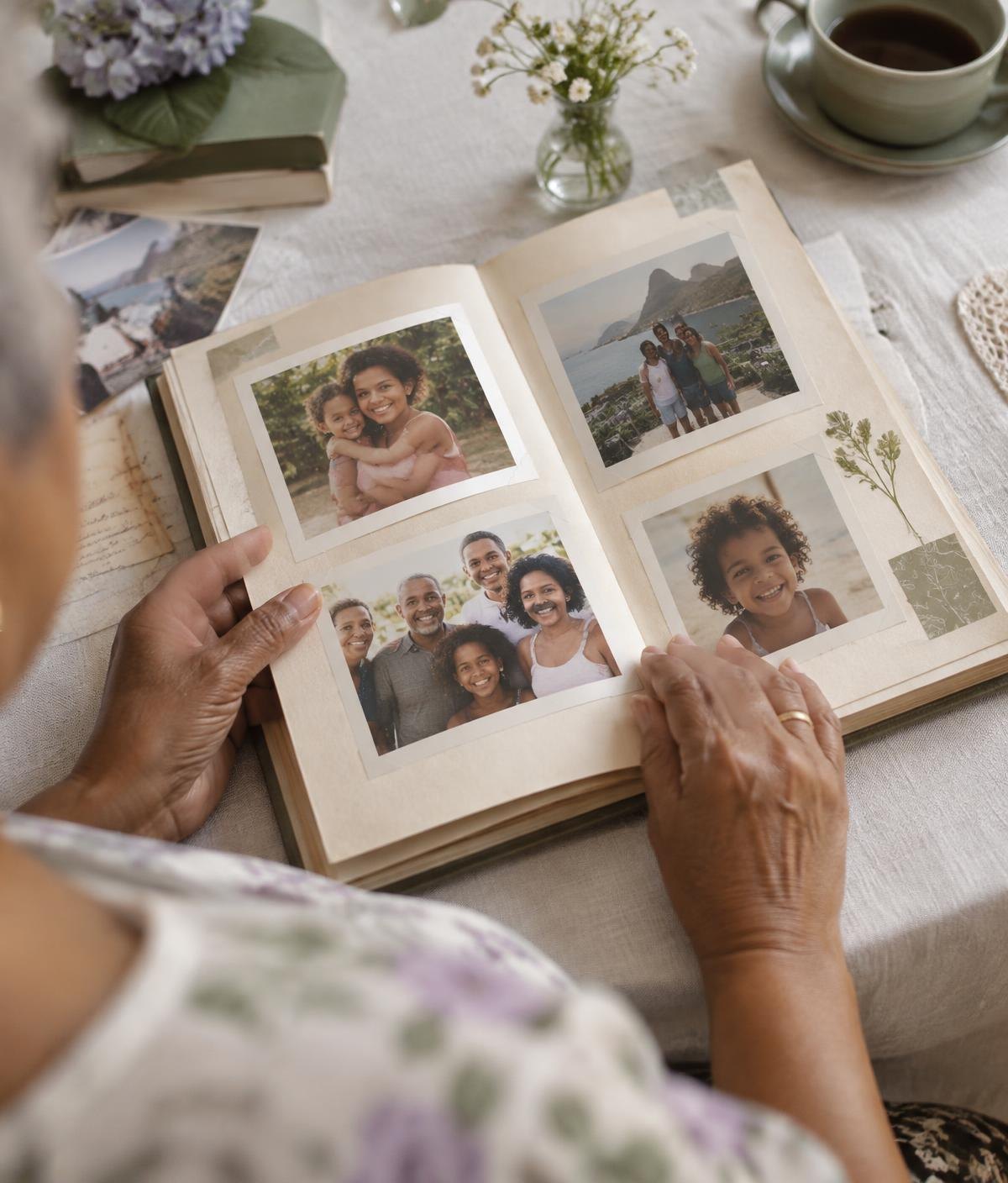 Mãos folheando um álbum com fotografias de uma família brasileira de diferentes gerações.